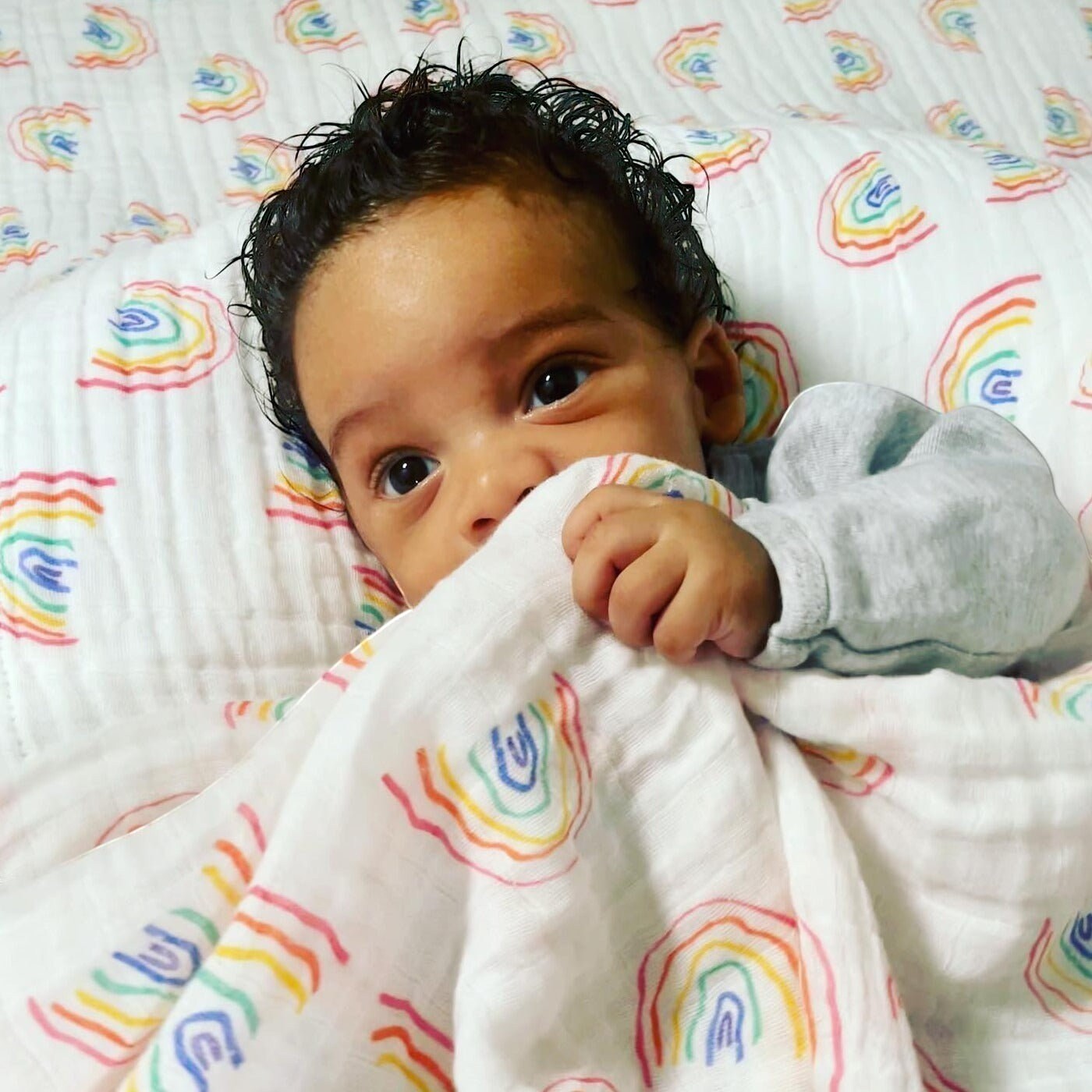 Precious Days Gifts rainbow muslin blanket with a baby wrapped in it. 100% cotton, 120cm x 120cm.