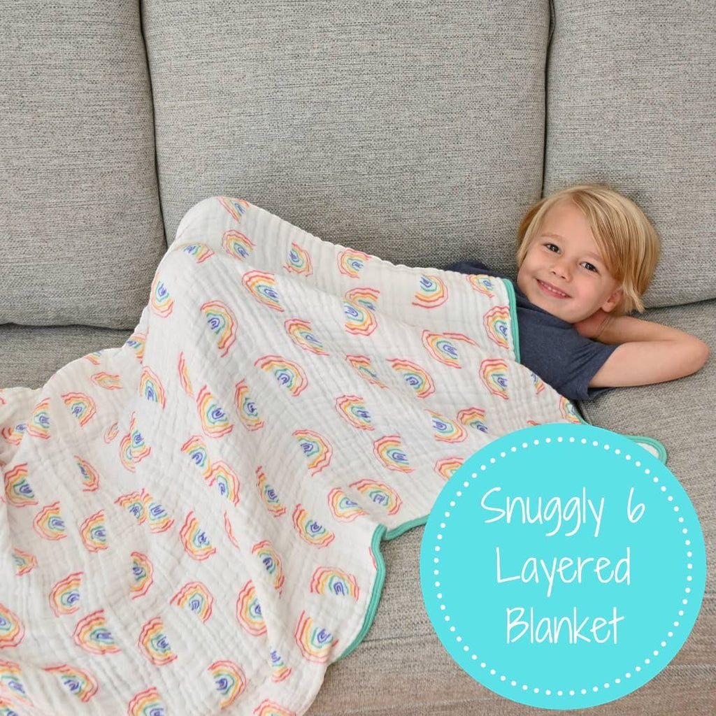 Precious Days Gifts 6-layer 100% cotton muslin quilt with a hand-drawn rainbow pattern and teal trim. A young boy is snuggled under it on a sofa.