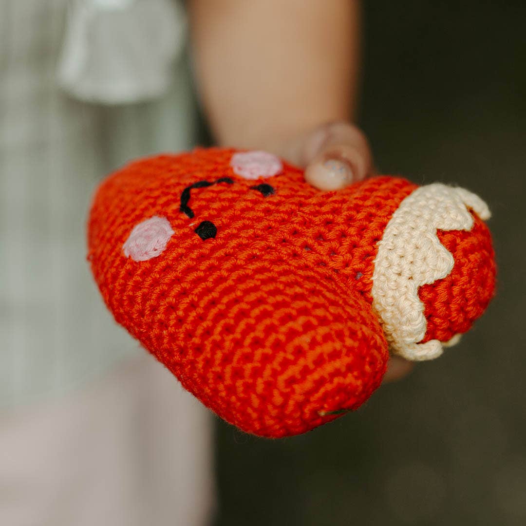 Precious Days Gifts red crochet heart rattle with a cute embroidered face held in a child's hand