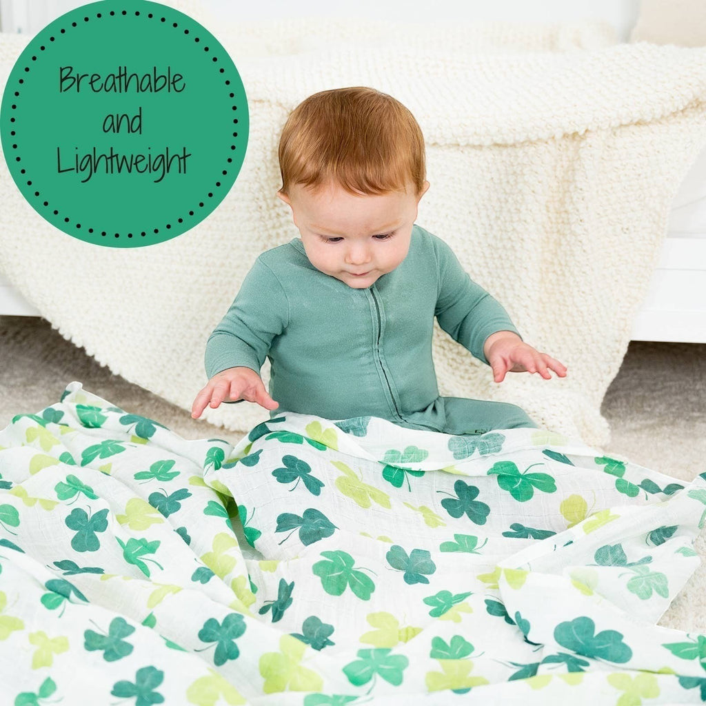 Precious Days Gifts baby sitting on a soft white blanket with a breathable cotton shamrock muslin swaddle