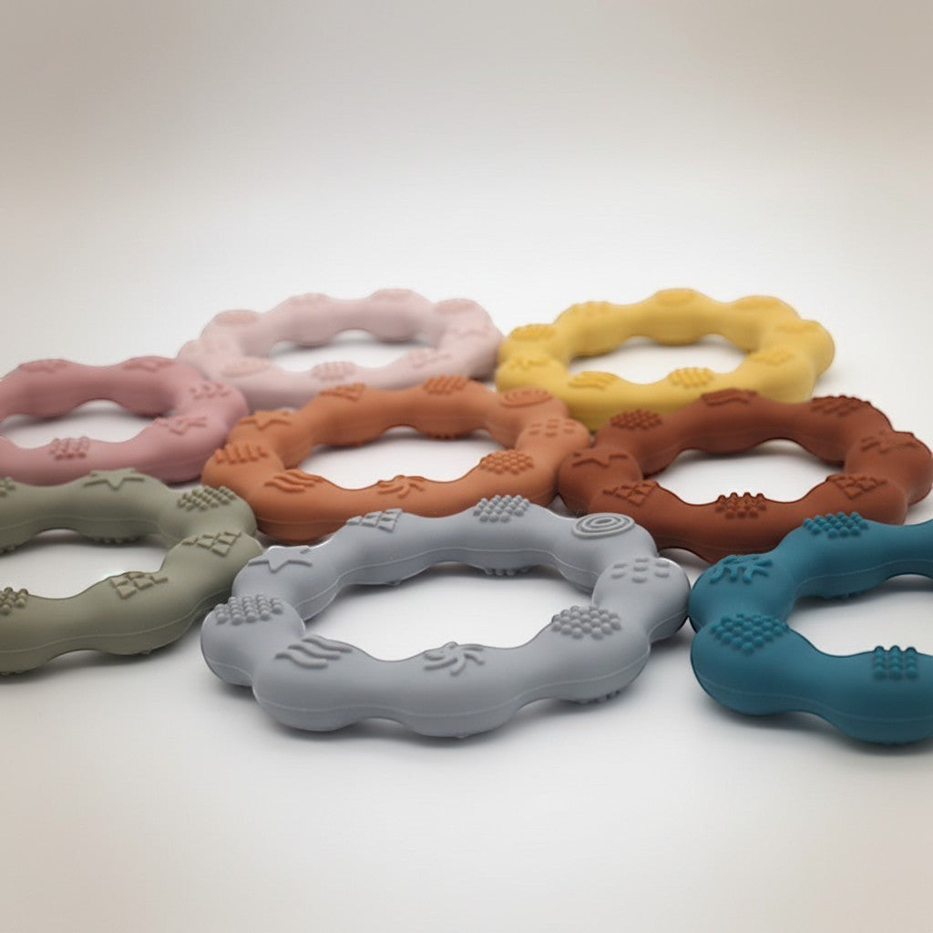 Precious Days Gifts set of silicone baby teethers in pastel pink, mustard yellow, terracotta, grey, and teal with textured surfaces.