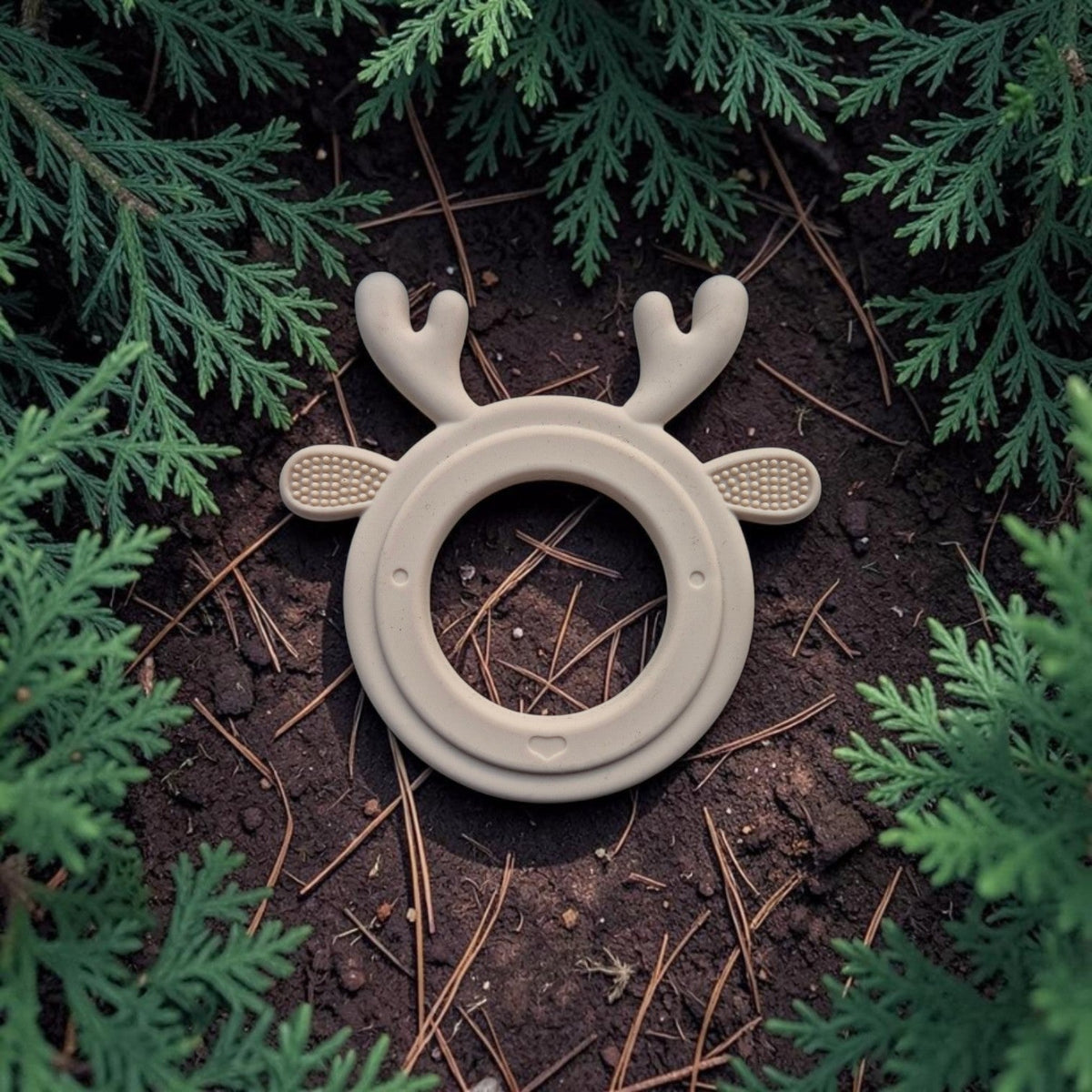 Precious Days Gifts beige silicone reindeer teether with textured surfaces for baby gum relief on a forest floor