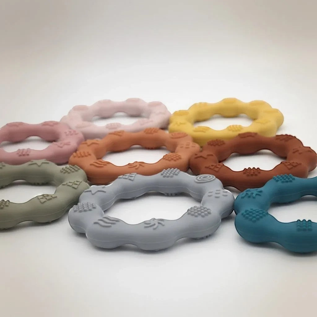 Precious Days Gifts silicone teethers in various pastel colors with textured surfaces for babies.