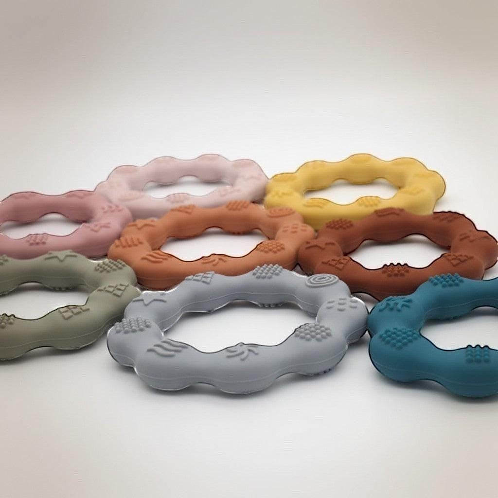 Precious Days Gifts set of 7 colorful silicone teething rings with textured surfaces for babies.