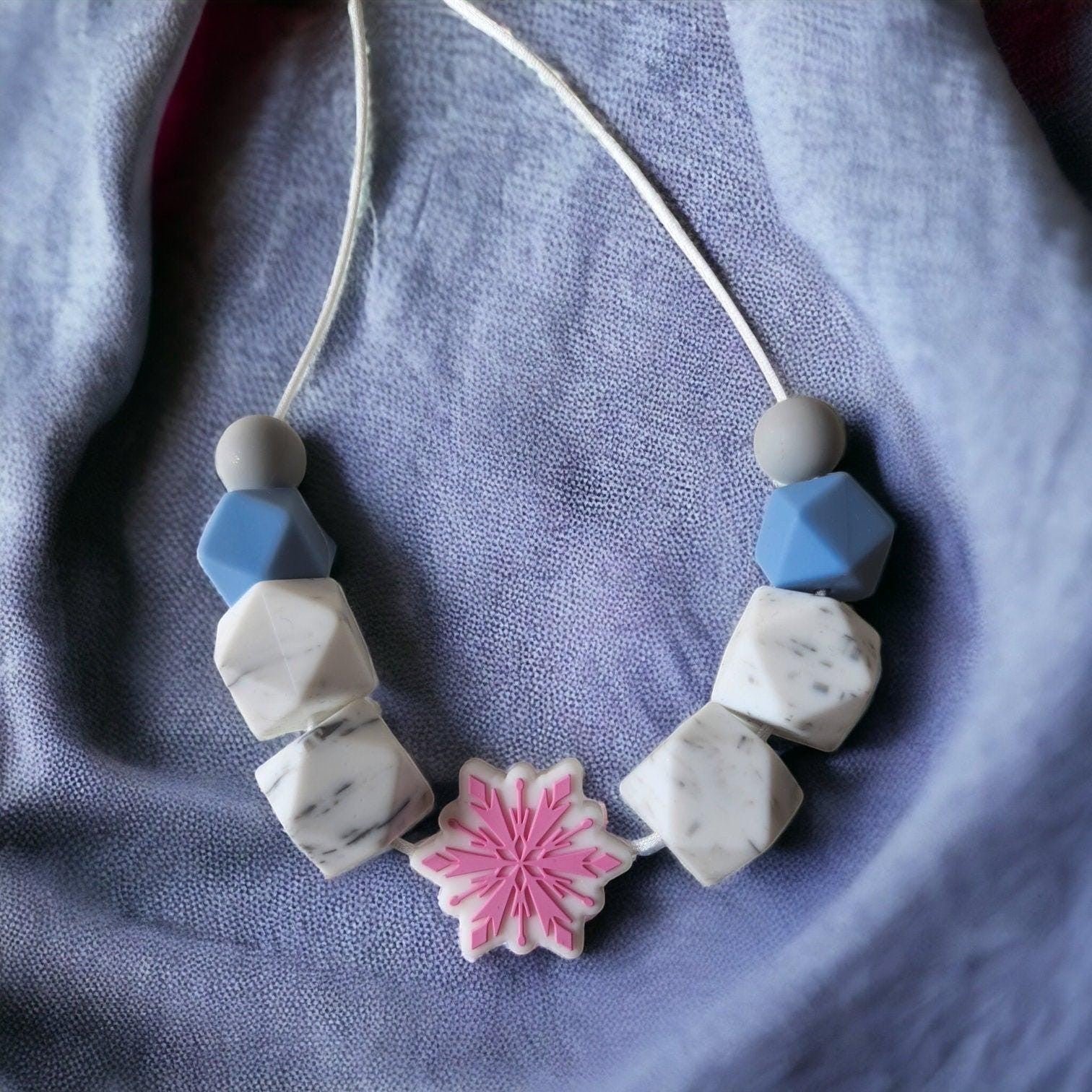 Precious Days Gifts snowflake teething necklace with white marble, blue, and grey silicone beads.