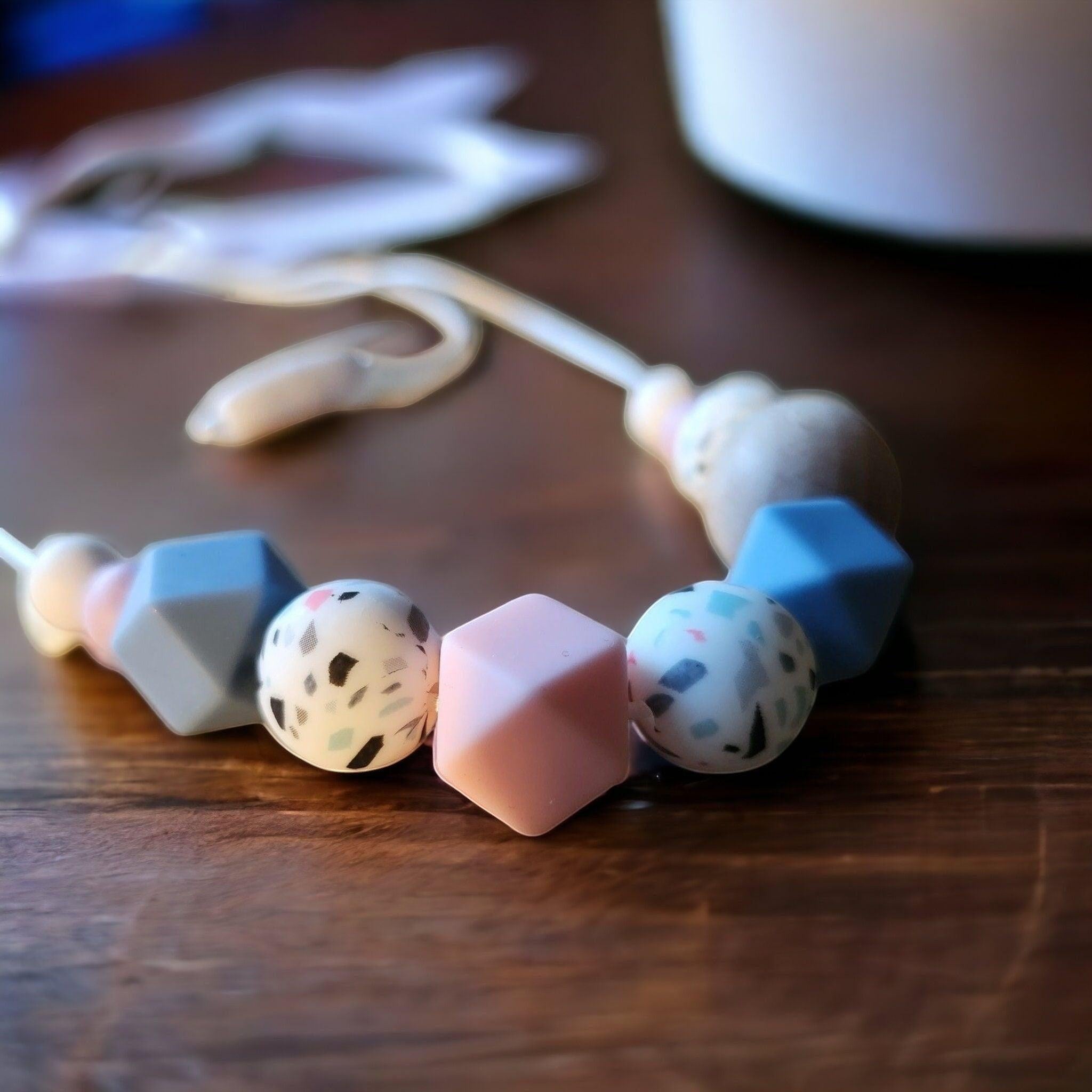 Precious Days Gifts speckled pastel silicone and wood teething necklace with pastel pink, blue, and speckled beads.