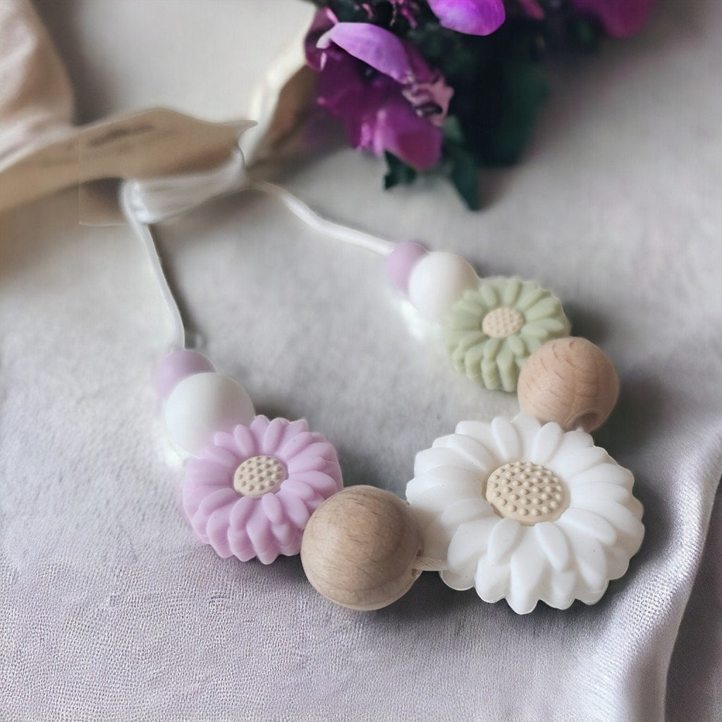 Precious Days Gifts Spring Daisy teething necklace with silicone and wood beads in pastel pink, green, white, and natural wood.