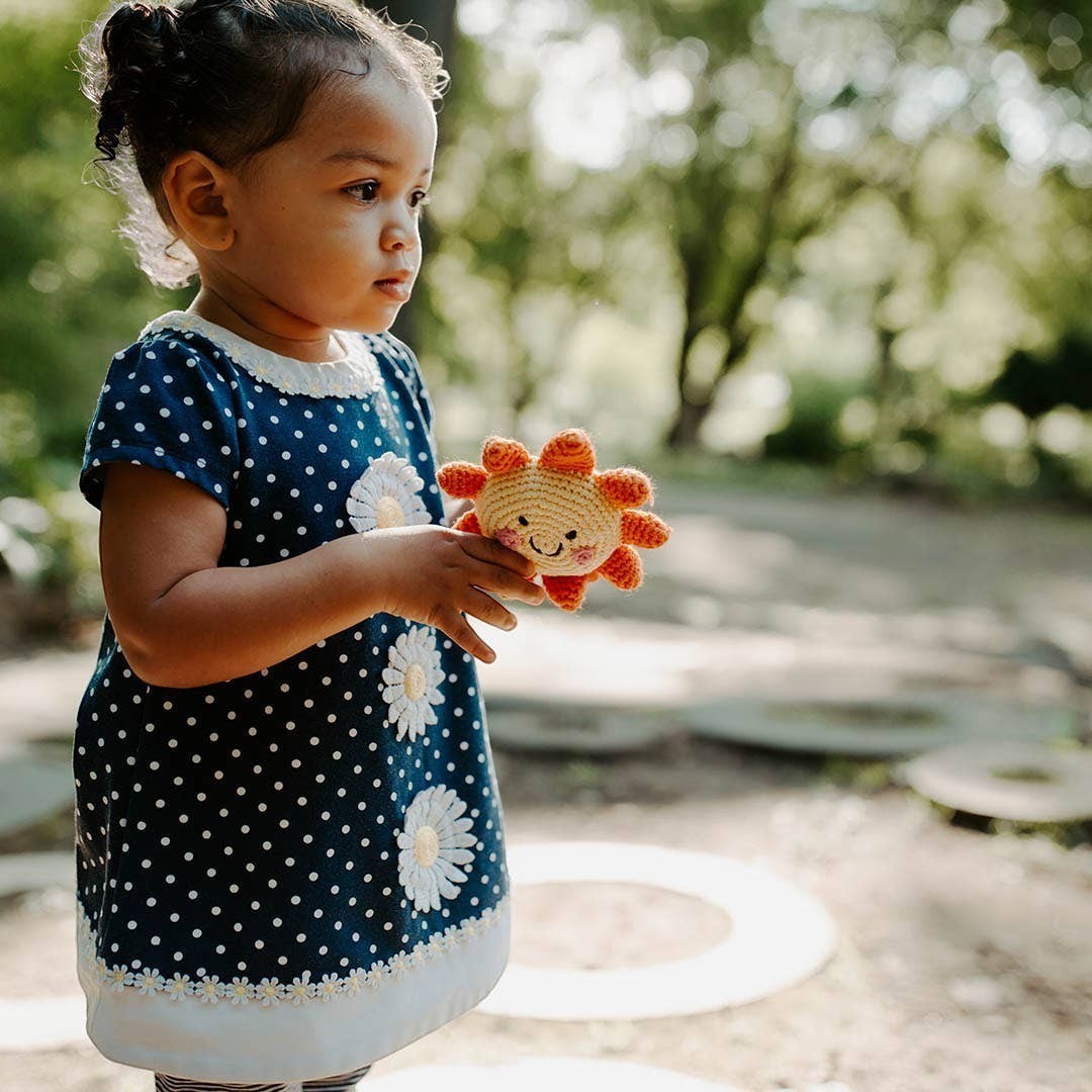 Toddler holding a handmade Precious Days Gifts sun rattle in a sunny outdoor setting