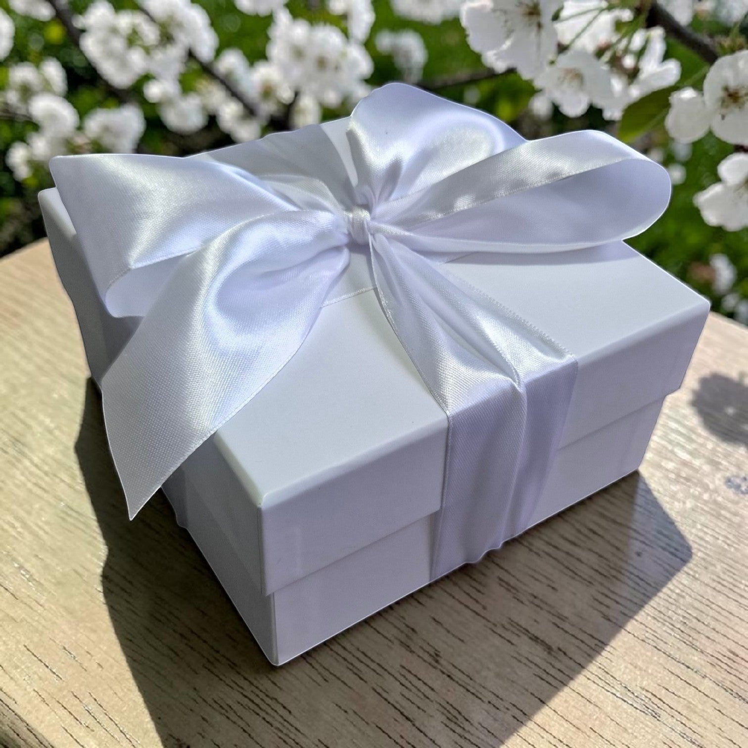 Precious Days Gifts Sunshine baby gift box in white with a satin ribbon bow, set against a backdrop of white flowers.