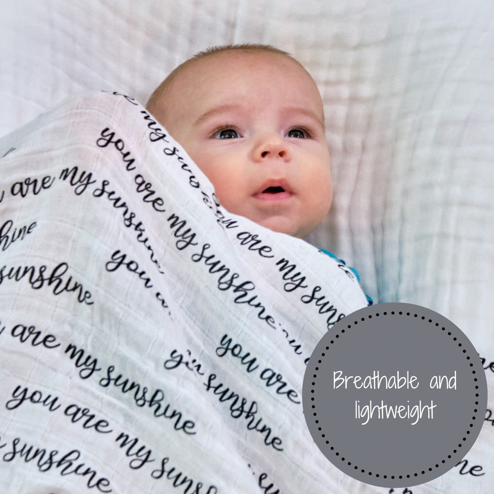 Precious Days Gifts baby swaddled in a soft white cotton muslin blanket with You Are My Sunshine text print