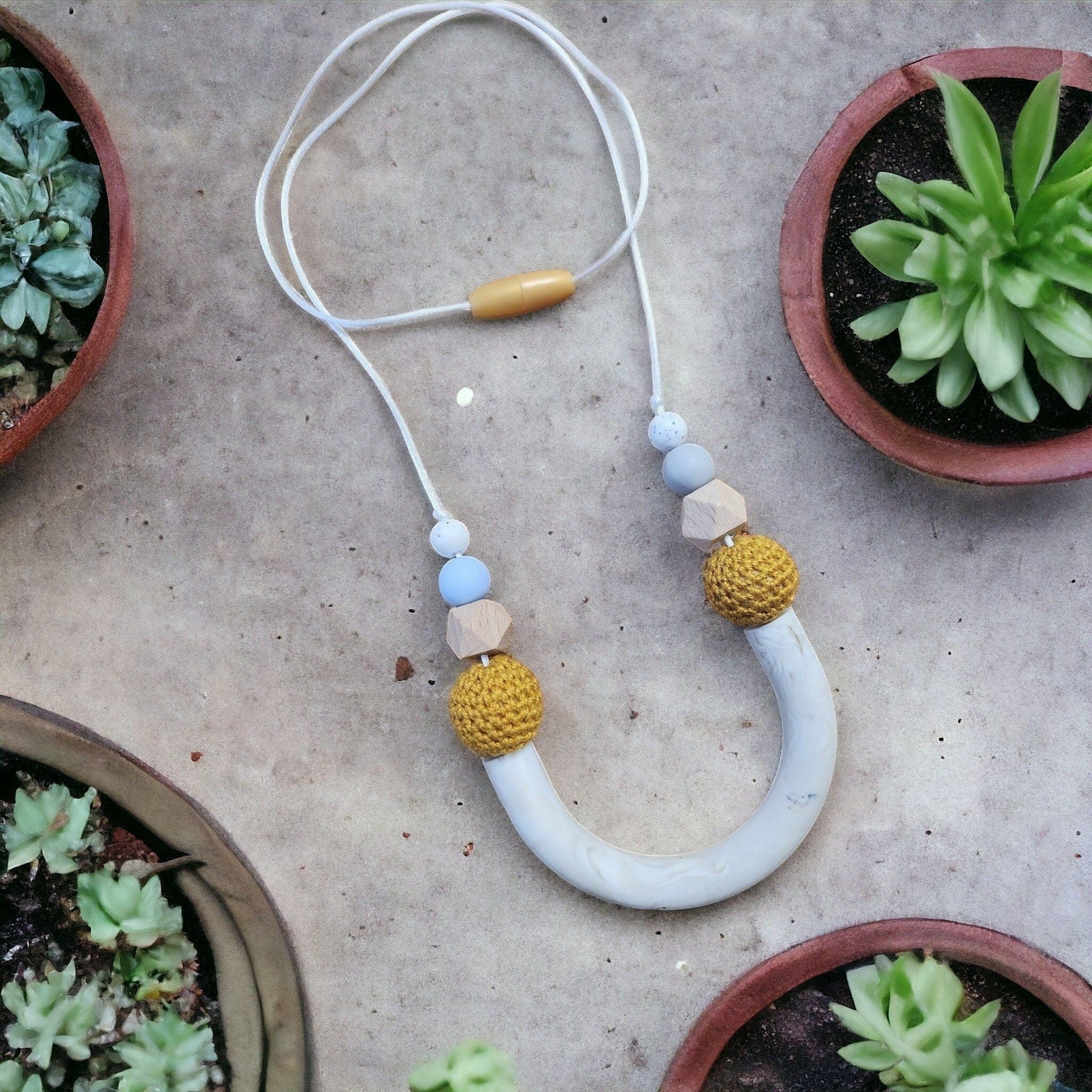 Precious Days Gifts U-shape teething necklace with silicone, wood, and crocheted beads in white, blue, yellow, and natural wood.