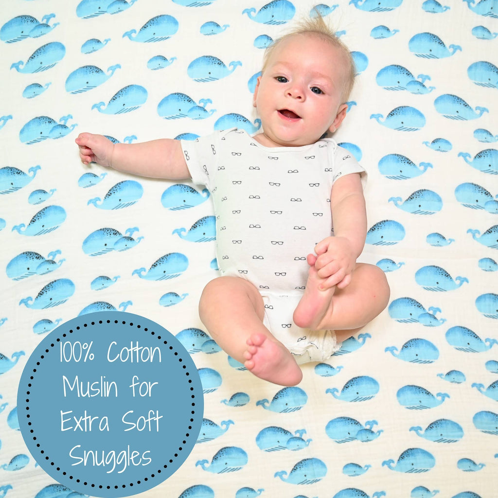 Precious Days Gifts baby swaddle blanket in 100% cotton muslin with a blue whale print. Baby wearing a white onesie with glasses print.